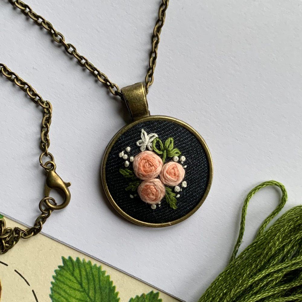 Apaļš kulons ar izšūtiem ziediņiem ķēdītē
