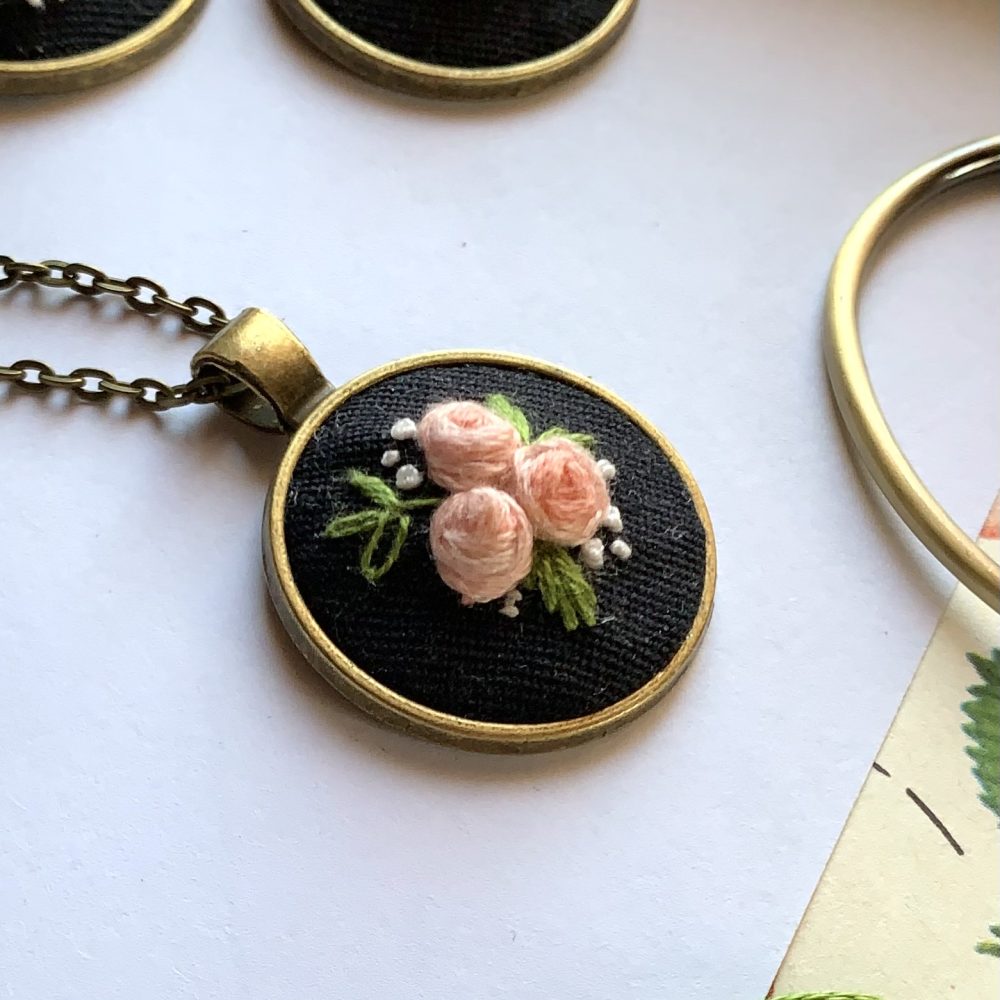 Apaļš kulons ar izšūtām rozītēm ķēdītē