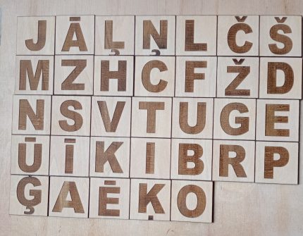 Koka magnētiskās burtiņu flīzes ar latviešu alfabēta burtiem, redzami dažādi latviešu valodas specifiskie burti.