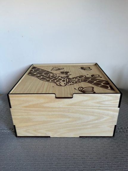 Koka kastīte ar gravētu žirafes un tauriņu dizainu uz vāka, aizvērta.