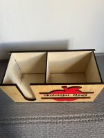 Koka galda organizators ar personalizētu uzrakstu "Skolotājai Ilzei", ar sarkanu ābola dekori un krāsainiem zīmuļiem iekšpusē, novietots uz rakstāmgalda.