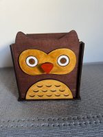 Koka pildspalvu turētājs pūces formā ar saulesbrillēm, piepildīts ar krāsainiem zīmuļiem. Koka pildspalvu turētājs pūces formā, bez piederumiem, ar dzeltenu vēderiņu un oranžu knābi.