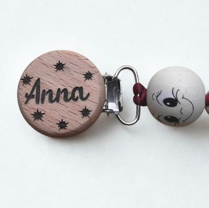 Koka knupīša turāmais ar emocionālām pērlītēm un personalizētu vārdu “Anna”, ar bordo aukliņu un metāla klipsi, novietots uz balta fona.