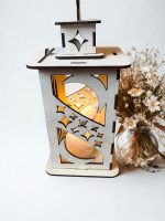 Koka dekoratīva laterna ar izgrieztiem mēness un zvaigžņu elementiem, ar siltu gaismu iekšpusē.