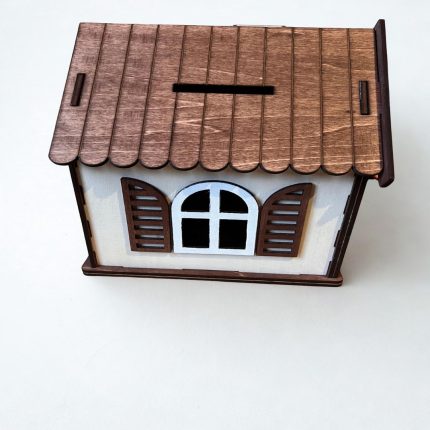 Koka naudas kaste mājiņas formā ar dekoratīvu logu un slēģiem, izgatavota ar lāzergriezumu.