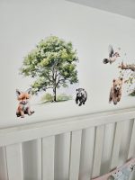 Meža dzīvnieku līmpapīra sienas uzlīmes bērnu istabā – lapsa, lācis, stirna, putni un koki izvietoti bērnu gultiņas garumā uz gaišas sienas.