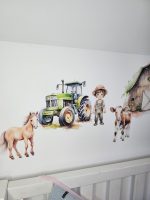 Fermas dzīvnieku līmpapīra sienas uzlīmes bērnu istabā ar govi, jēru, kazlēnu, cālīti, kaķēnu un fermas ēkām, izvietotas virs bērnu gultiņas.