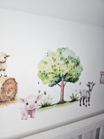 Fermas dzīvnieku līmpapīra sienas uzlīmes bērnu istabā ar govi, jēru, kazlēnu, cālīti, kaķēnu un fermas ēkām, izvietotas virs bērnu gultiņas.