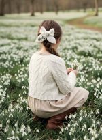 Balta lina matu bante ar izšūtām sniegpulkstenītēm meitenes bizē pavasara fotosesijā starp sniegpulkstenītēm.