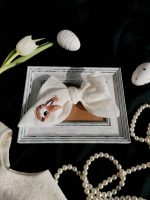 Balta lina matu bante ar izšūtu zaķīti un cirkonija pērlītēm, stilizēta Lieldienu fotosesijas kompozīcija ar baltu tulpi un dekoratīvām olām.