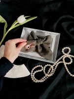 Rokā turēta olīvzaļa lina matu bante ar zaķa izšuvumu un cirkonija pērlītēm svētku kompozīcijā.