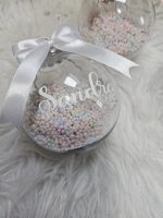 Personalizēti Ziemassvētku eglītes rotājumi ar vārdu, caurspīdīgas Ziemassvētku bumbas 8 cm diametrā ar krāsainu putuplasta bumbiņu pildījumu un dekoratīvu lentīti, pieejami 3 personalizācijas krāsās. Oriģināla Ziemassvētku dāvana bērniem un ģimenei. Personalizēti rotājumi. Eglītes bumbas